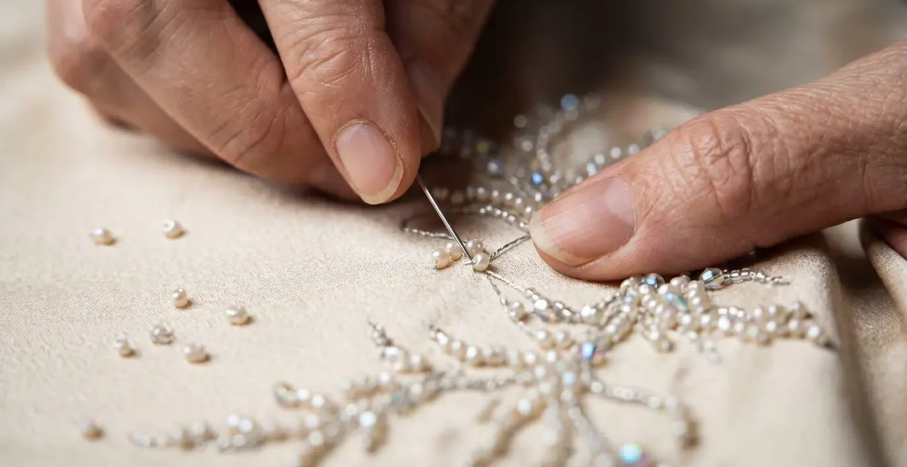Detailaufnahme von Händen bei feiner Perlenstickerei an einem Haute-Couture-Kleidungsstück